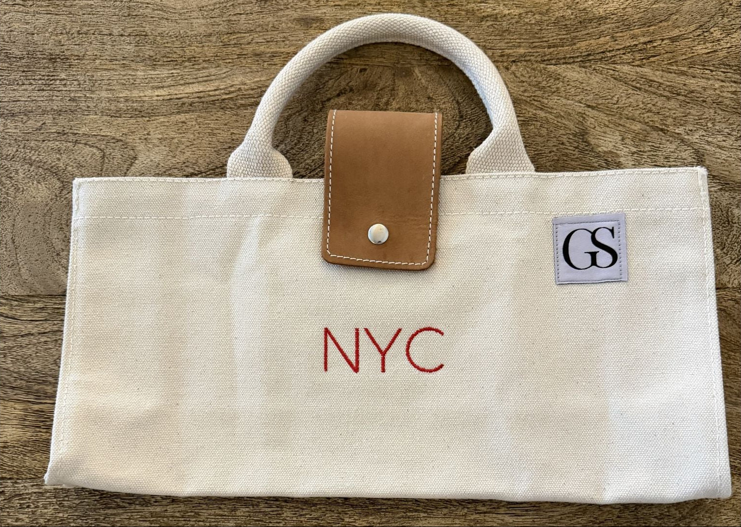 White tote bag with 'NYC' and initials 'GS' on a wooden surface