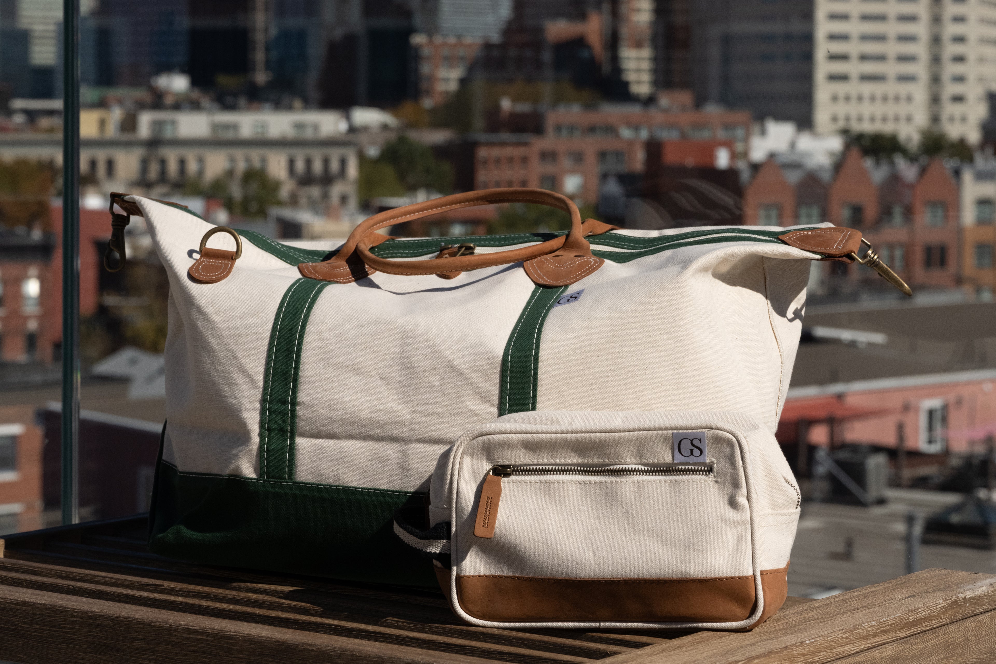 White duffel bag with green straps and brown accents on a rooftop with cityscape background